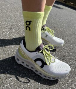 WhatsApp_Image_2024-11-15_at_15.57.52 | UAE SPORT STORE Person wearing white On running sneakers with lime green laces and bright yellow socks standing on asphalt road.