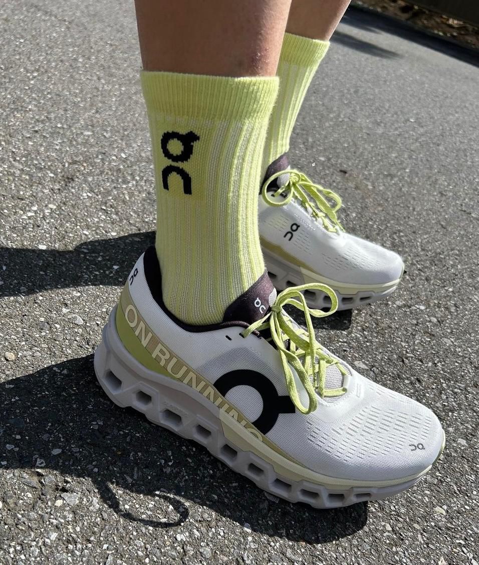 WhatsApp_Image_2024-11-15_at_15.57.52 | UAE SPORT STORE Person wearing white On running sneakers with lime green laces and bright yellow socks standing on asphalt road.
