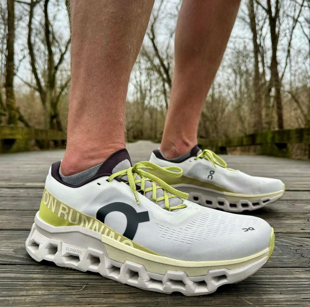 WhatsApp_Image_2024-11-15_at_15.57.54 | UAE SPORT STORE Close-up of white On running shoes with lime green laces on a wooden boardwalk.
