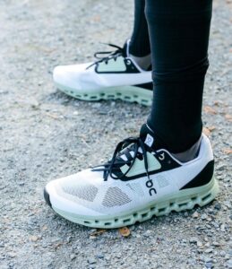 Person wearing white and mint-green running shoes on a gravel path, legs in black leggings ready to run