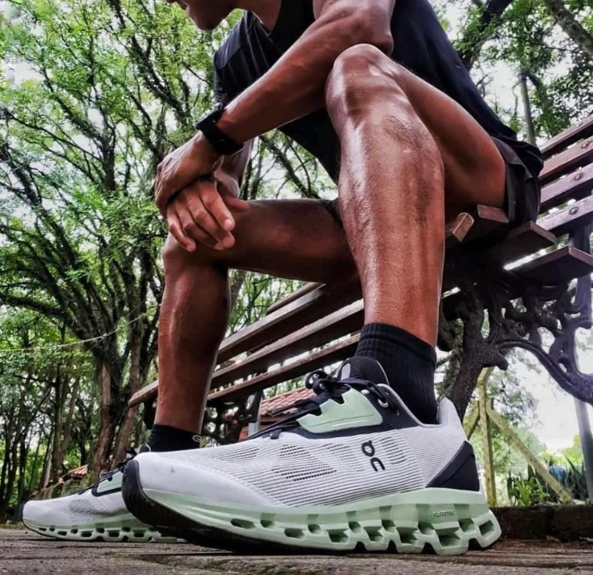 WhatsApp_Image_2024-11-21_at_13.48.47 Close-up of a person tying the laces of white mint trail running shoes while sitting on a park bench outdoors.