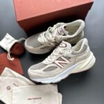 WhatsApp_Image_2024-12-04_at_12.23.53 | UAE SPORT STORE Beige New Balance sneakers with white soles, placed on a dark surface beside a brown box and dust bags. Visible burgundy NB logo on the side and tongue label.