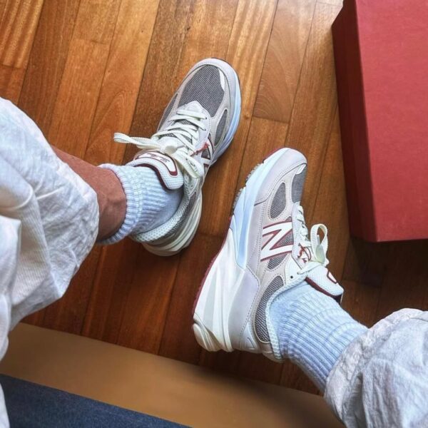 Person wearing white and gray athletic shoes with light blue socks, resting feet on a hardwood floor near a red box.“