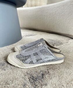 Pair of gray knitted slip-on sneakers with white soles resting on a light gray carpet near a gray furniture leg.