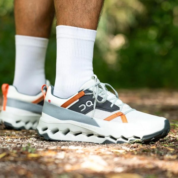 Pair of white and gray running shoes with orange accents on a trail, worn with white socks.