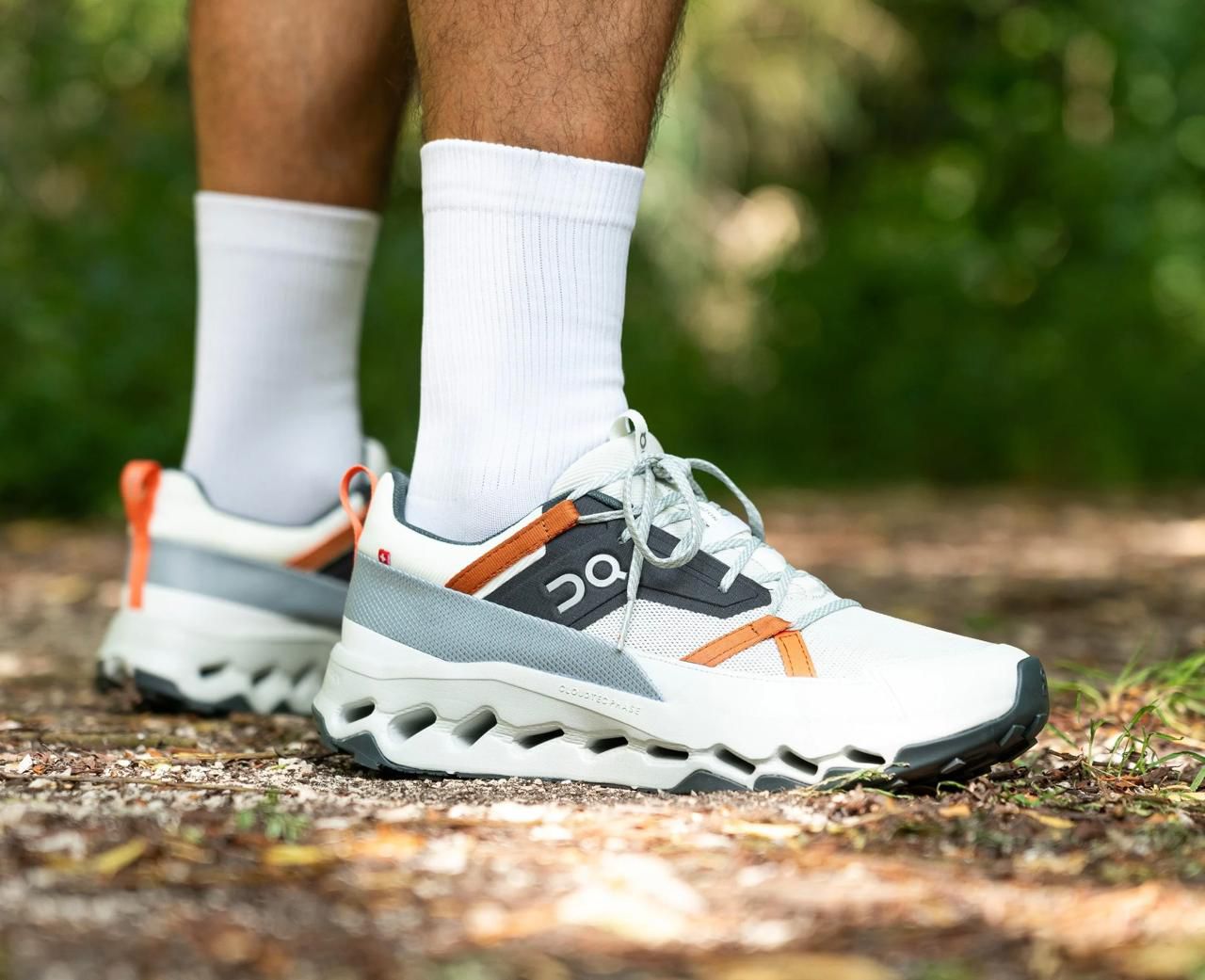 WhatsApp_Image_2024-12-06_at_14.41.58 Pair of white and gray running shoes with orange accents on a trail, worn with white socks.
