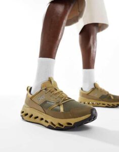 Low-angle shot of a person wearing tan-brown running shoes with a chunky, sculpted sole and white socks.