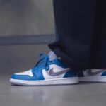 Blue and white Nike sneakers worn with dark jeans, close-up side view on a gray floor