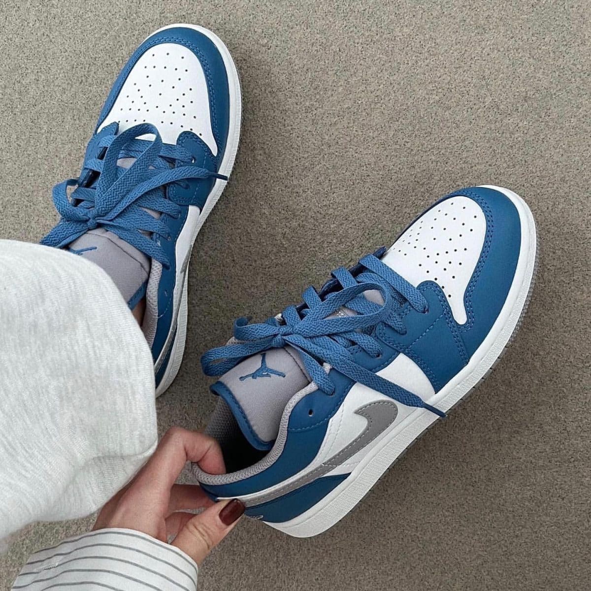 Blue and white sneakers on a beige carpet, with a person tightening the laces.