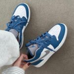 Blue and white sneakers on a beige carpet, with a person tightening the laces.