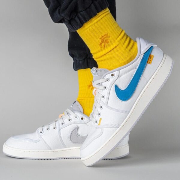 White Nike sneakers with a blue Swoosh, shown in side view with bright yellow socks and dark pants visible.