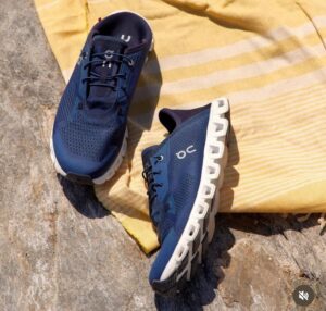 Pair of blue running shoes with white cushioned soles resting on a rocky surface beside a yellow striped towel.
