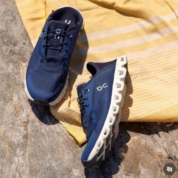 Pair of blue running shoes with white cushioned soles resting on a rocky surface beside a yellow striped towel.