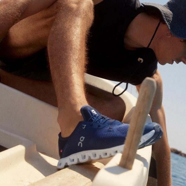 Person wearing a blue athletic shoe stepping onto a boat near the water, sunlit scene.