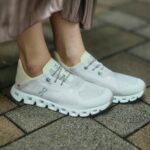 White athletic sneakers worn by a person, standing on a brick pavement surface.