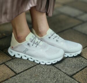 WhatsApp_Image_2024-12-14_at_14.16.10 | UAE SPORT STORE White athletic sneakers worn by a person, standing on a brick pavement surface.