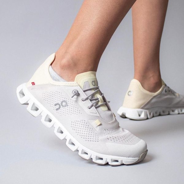 White/cream mesh running shoes with a chunky segmented sole, worn on a person’s feet.