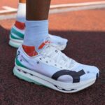 WhatsApp_Image_2024-12-15_at_10.40.38 | UAE SPORT STORE White athletic running shoe with teal, green, and orange accents on a red track, laces tied, paired with light blue socks (close-up).