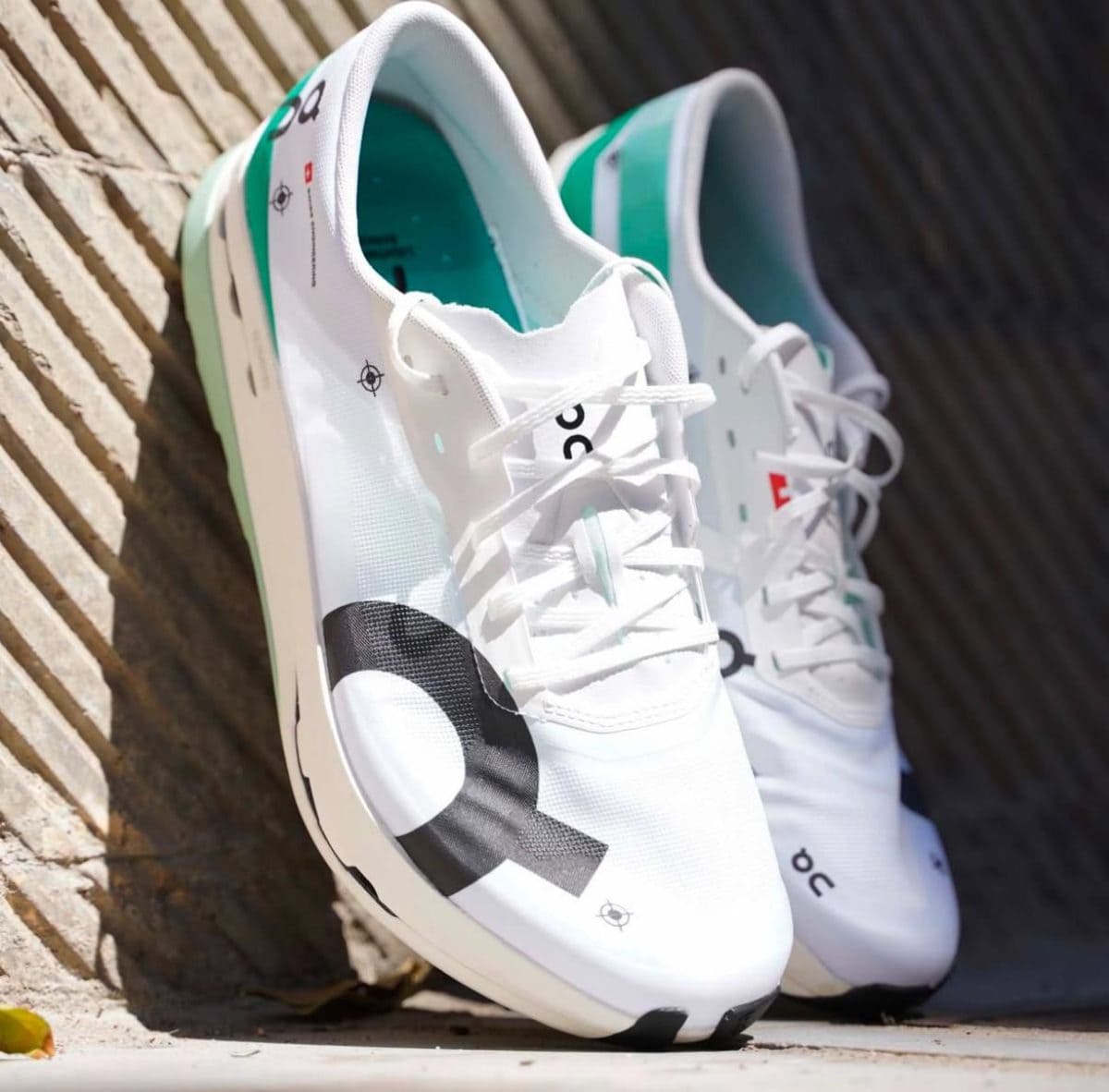 White On running shoes with teal interior and black logo, resting against a brick wall edge.