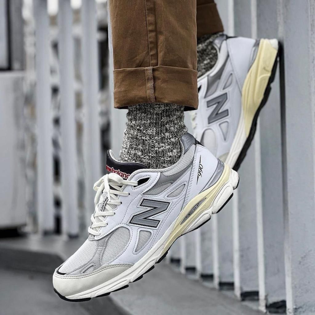 WhatsApp_Image_2024-12-18_at_11.32.37 Person wearing white/gray New Balance sneakers with chunky sole, gray knit socks, and rolled brown pants leaning on a metal railing