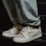 Close-up of pastel pink and beige sneakers on a person wearing gray sweatpants on a dark surface.