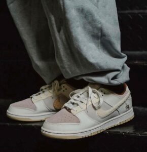 Close-up of pastel pink and beige sneakers on a person wearing gray sweatpants on a dark surface.