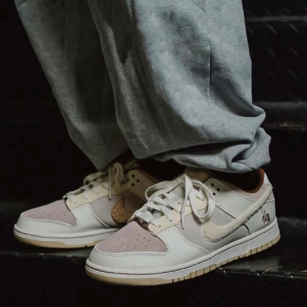Close-up of pastel pink and beige sneakers on a person wearing gray sweatpants on a dark surface.