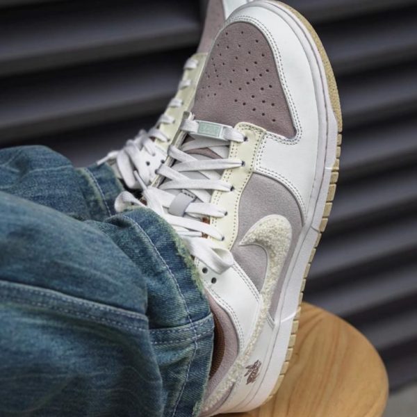 White and beige sneakers with perforated toe resting on a wooden stool, denim jeans visible at the cuff.