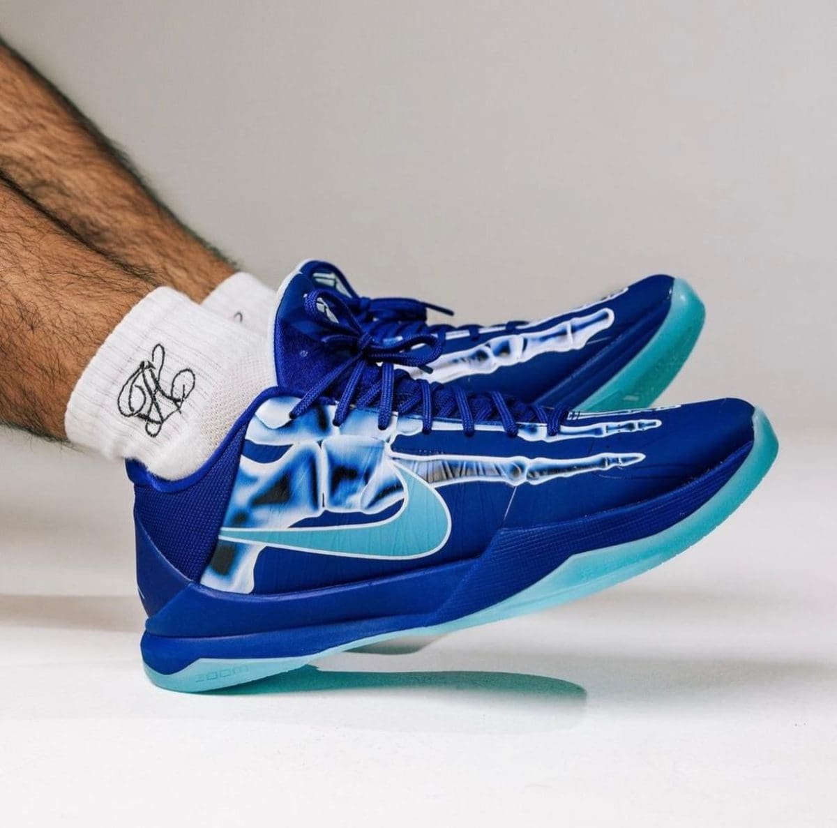 Blue Nike running shoes with turquoise soles worn by a person, mid-step with white socks showing.