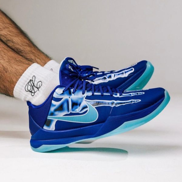 Blue Nike running shoes with turquoise soles worn by a person, mid-step with white socks showing.