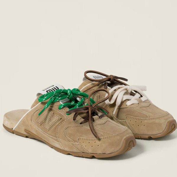 Beige suede sneakers with chunky soles and mismatched laces—green on the left shoe and white on the right.