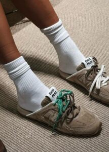 WhatsApp_Image_2024-12-30_at_12.17.00 | UAE SPORT STORE Person wearing white crew socks and beige sneakers with green laces on a carpeted floor, close-up of feet.