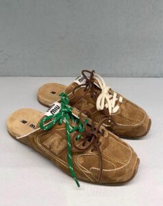 WhatsApp_Image_2024-12-30_at_14.44.35 | UAE SPORT STORE Brown suede sneakers with multicolored laces (green on the left, white/brown on the right) on a light surface.