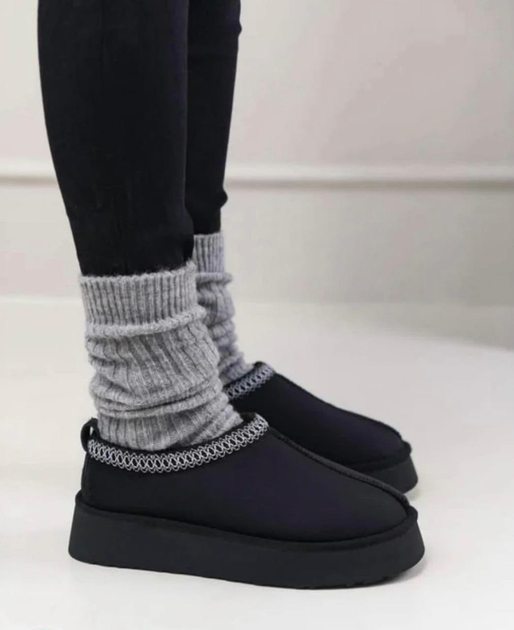 WhatsApp_Image_2025-01-10_at_12.27.38 | UAE SPORT STORE Feet wearing gray ribbed socks tucked into black platform clogs with a silver chain detail, standing on a light floor.