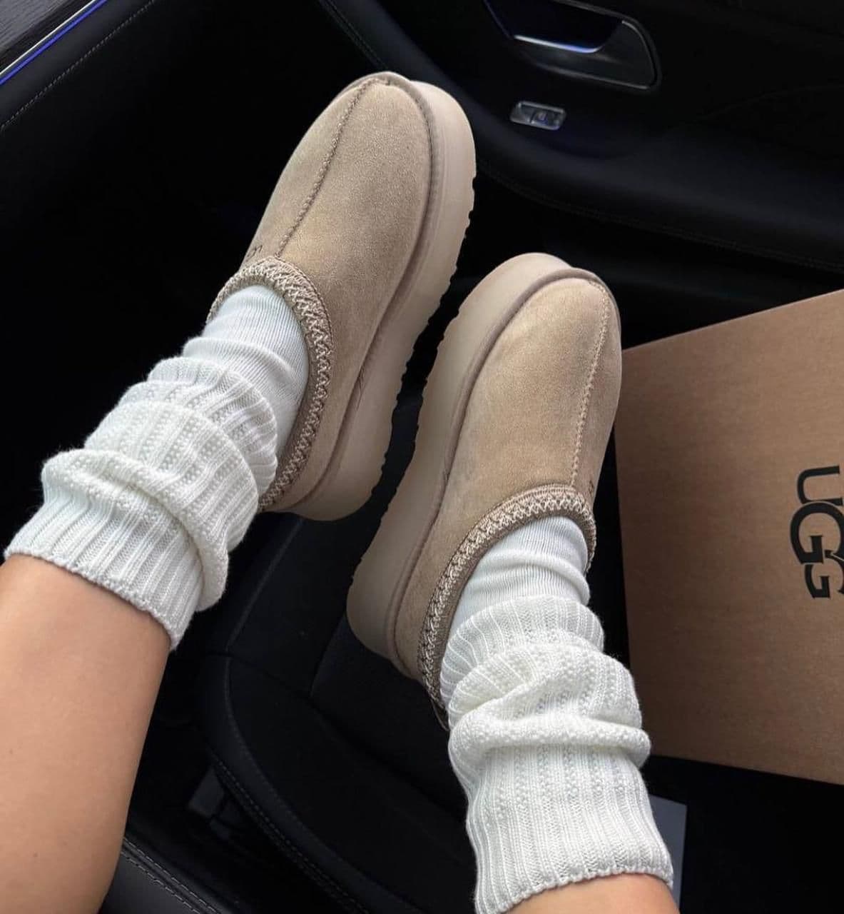 WhatsApp_Image_2025-01-10_at_15.30.34 | UAE SPORT STORE Beige suede slippers worn with white socks, resting in a car with a cardboard box nearby (UGG-like brand).