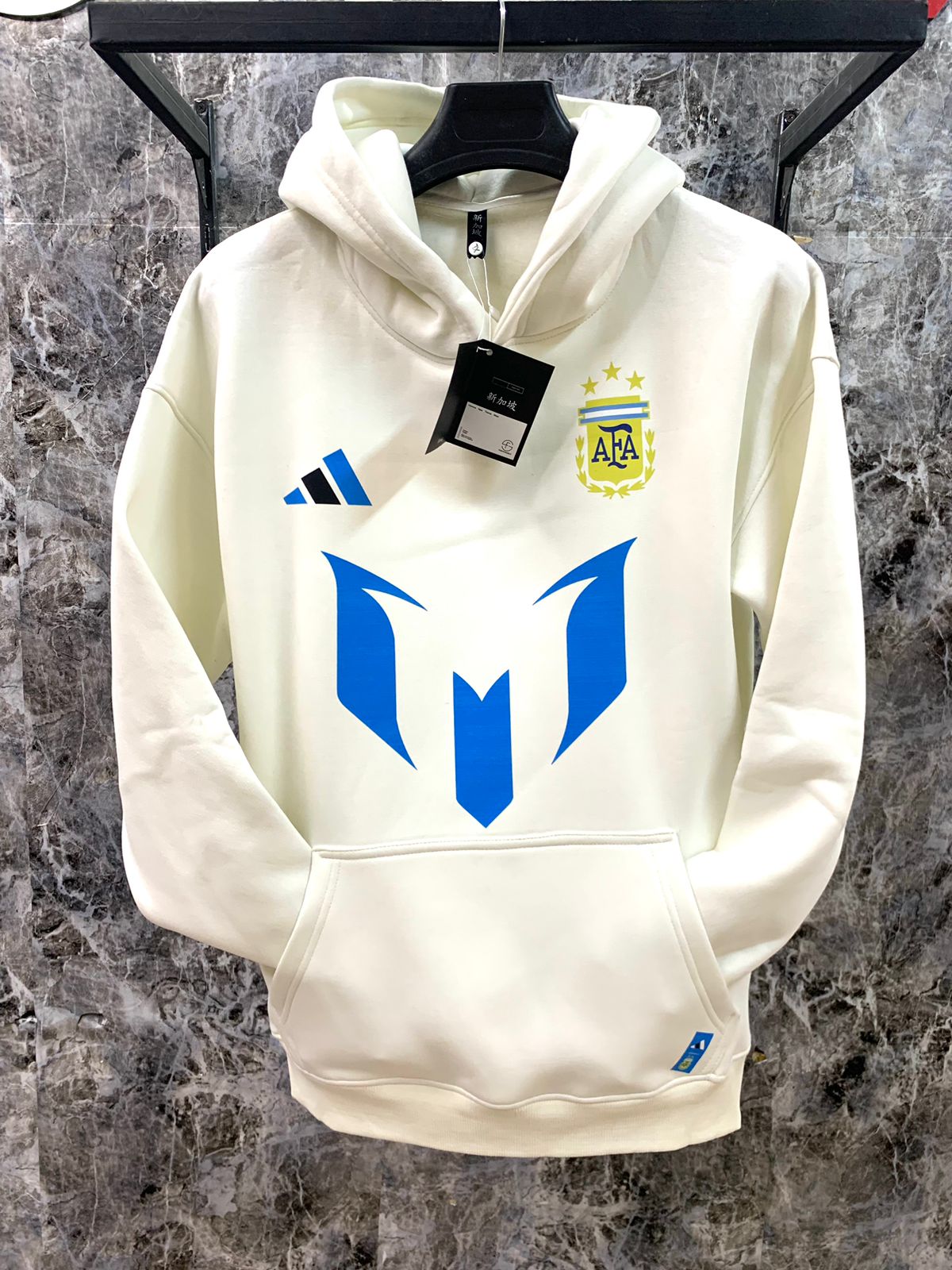 WhatsApp_Image_2025-01-10_at_18.38.57_1 | UAE SPORT STORE Cream-white hoodie on a hanger with a bold blue geometric 'M' logo prominently on the front, an Adidas logo on the left chest, and a yellow AFA crest on the right chest.