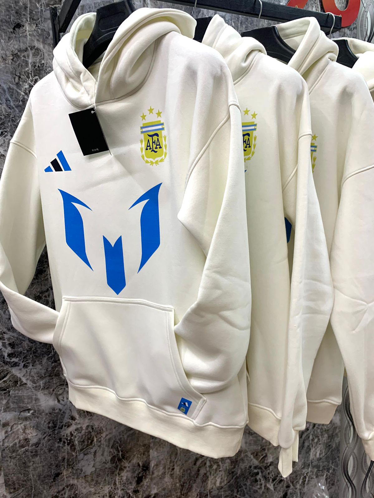 WhatsApp_Image_2025-01-10_at_18.38.57_3 | UAE SPORT STORE White hoodie on a rack featuring a blue shield-like logo on the front and a small crest with AFA letters on the chest.