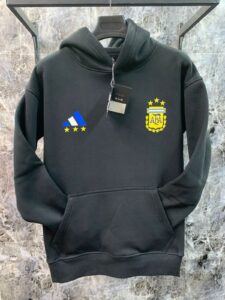 Black hoodie on a hanger with a blue Adidas-style logo and a yellow Argentina crest on the chest; tag hanging from the drawstring.