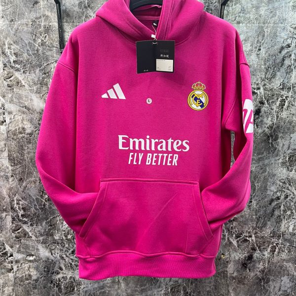 Bright pink Real Madrid hoodie on a hanger, showing Adidas logo, Real Madrid crest, and Emirates Fly Better branding with a front pocket.
