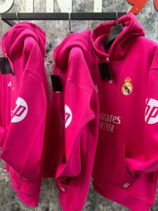 WhatsApp_Image_2025-01-10_at_18.40.06 | UAE SPORT STORE Bright pink Real Madrid hoodies on a rack, showing the club crest on the chest and Emirates sponsor text.