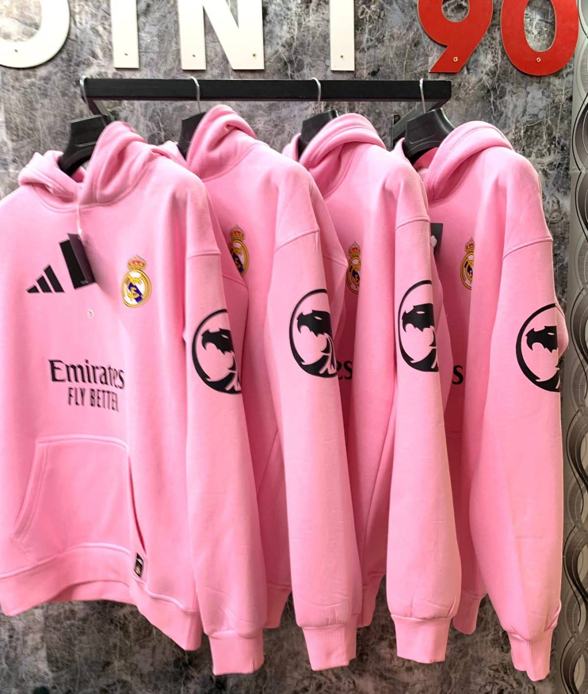 Row of pink Real Madrid hoodies on a rack, showing the club crest and Emirates Fly Better sponsor logo