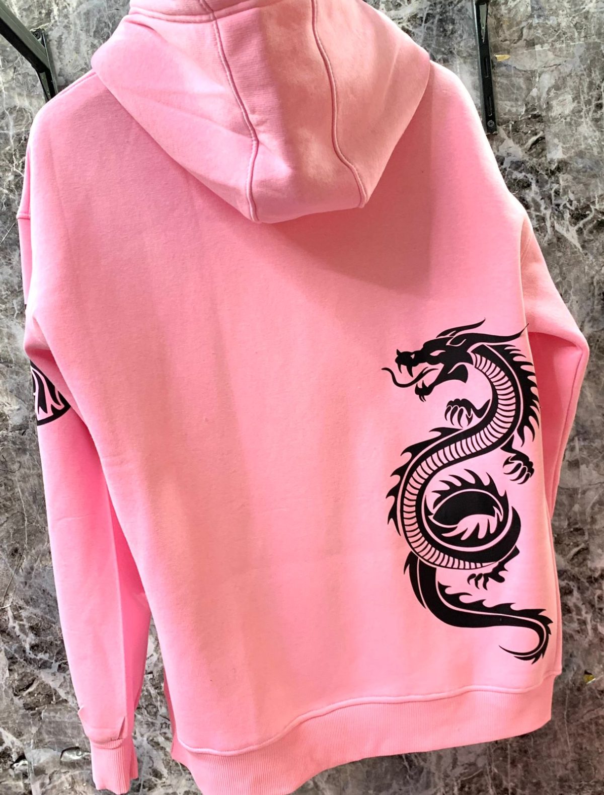 Back view of a pink hoodie with a bold black dragon graphic along the lower right back.