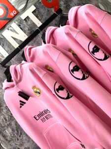 Row of pink hoodies hanging on a rack, each with the Real Madrid crest and Emirates Fly Better text visible on the front.