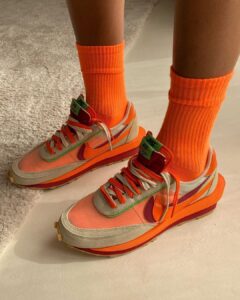 Pair of bright orange and peach Nike sneakers with lime green accents, worn with matching orange crew socks on a pale floor.
