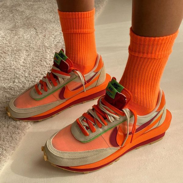 Pair of bright orange and peach Nike sneakers with lime green accents, worn with matching orange crew socks on a pale floor.