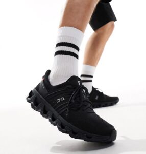 Close-up of a black running shoe with a chunky segmented sole on a person wearing white crew socks with black stripes, mid-step motion.