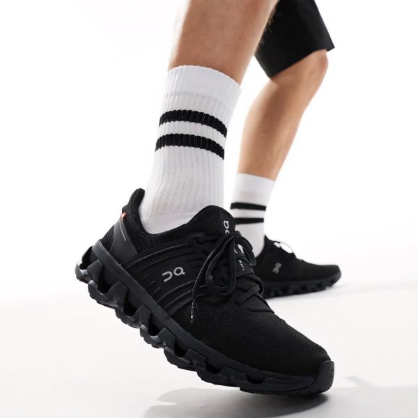 Close-up of a black running shoe with a chunky segmented sole on a person wearing white crew socks with black stripes, mid-step motion.