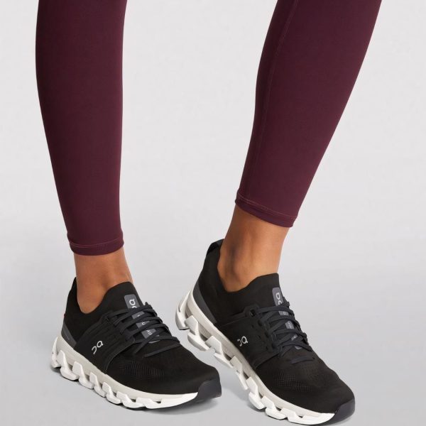 Person wearing black athletic sneakers with a white chunky sole, paired with burgundy leggings, standing on a light background.