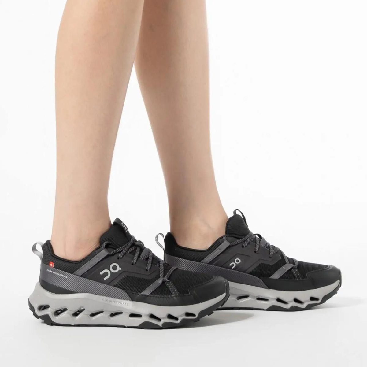 Pair of black and gray On Running Cloud sneakers on a person’s feet against a white background