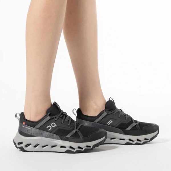Pair of black and gray On Running Cloud sneakers on a person’s feet against a white background